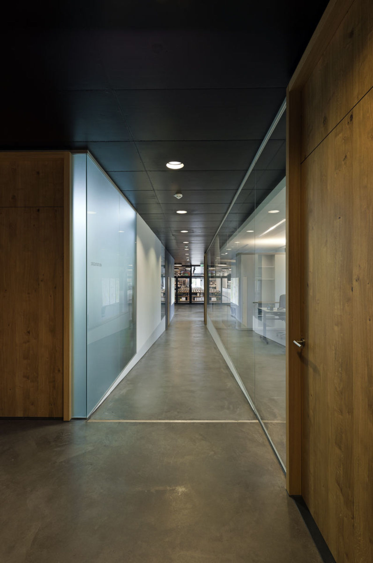 Foto: Blick in die Flure des Obergeschosses, die durch eine Glaswand die Büros abgrenzt. Die Büros werden durch Türen aus hellen Holz erschlossen.