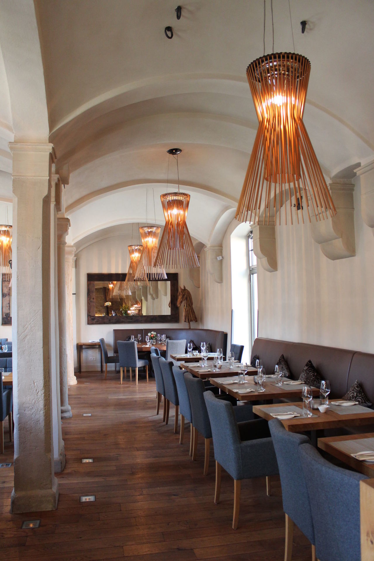 Foto: Restaurant mit dunklem Holzboden und einer Gewölbedecke, die auf rechteckigen Säulen aufliegt.