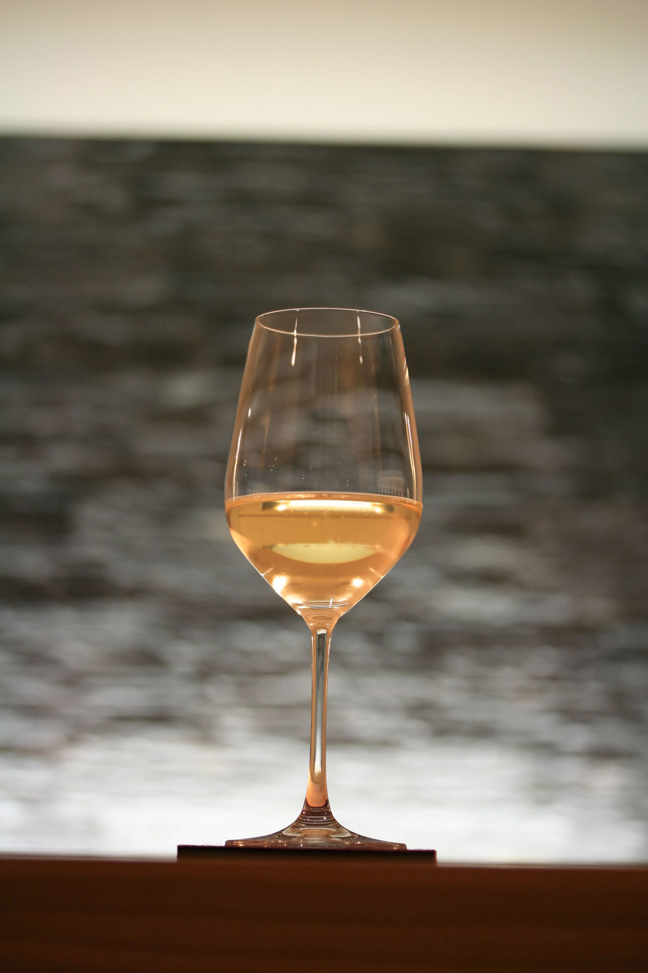 Foto: Nahaufnahme eines mit Burgunder gefüllten Weinglases vor einer grauen Steinwand.