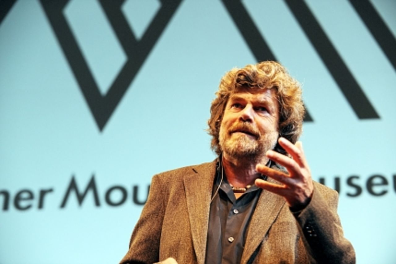 Foto: Im Vordergrund Reinhard Messner während seines Vortrages, im Hintergrund das Logo der Messner Mountain Museen