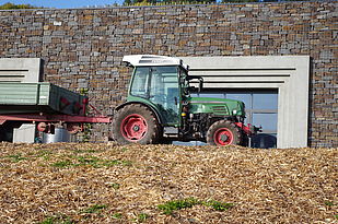 Ein Traktor vor dem neuen Wirtschaftsgebäude, das sich mit seiner Bruchsteinfassade und dem dem mit Beton eingefassten Toroptimal in die Landschaft einfügt.