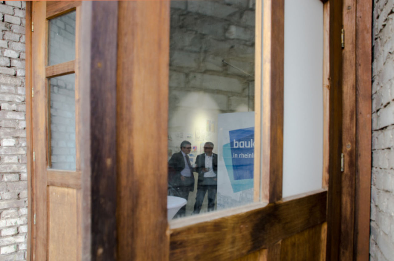 Eine geöffnete, hölzerne Tür, durch deren Verglasung der Blick ins Innere des Foyers der Bauausstellung geht.