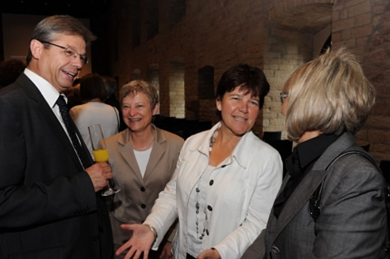 Foto: Vor der Veranstaltung angeregte Unterhaltung im Festsaal: Drei Frauen und ein Mann lachen.