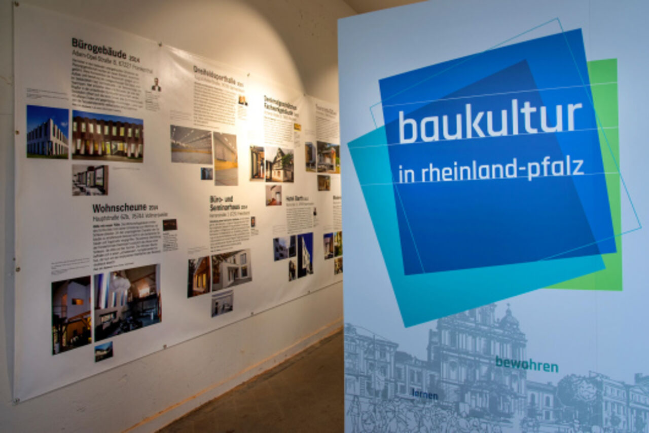 Blick in die Baukulturlounge, links im Bild sind die PVC-Planen zu sehen, auf denen Projekte dargestellt sind, rechts im Bild eine Sitzbankrückwand, auf der steht "baukultur in rheinland-pfalz"