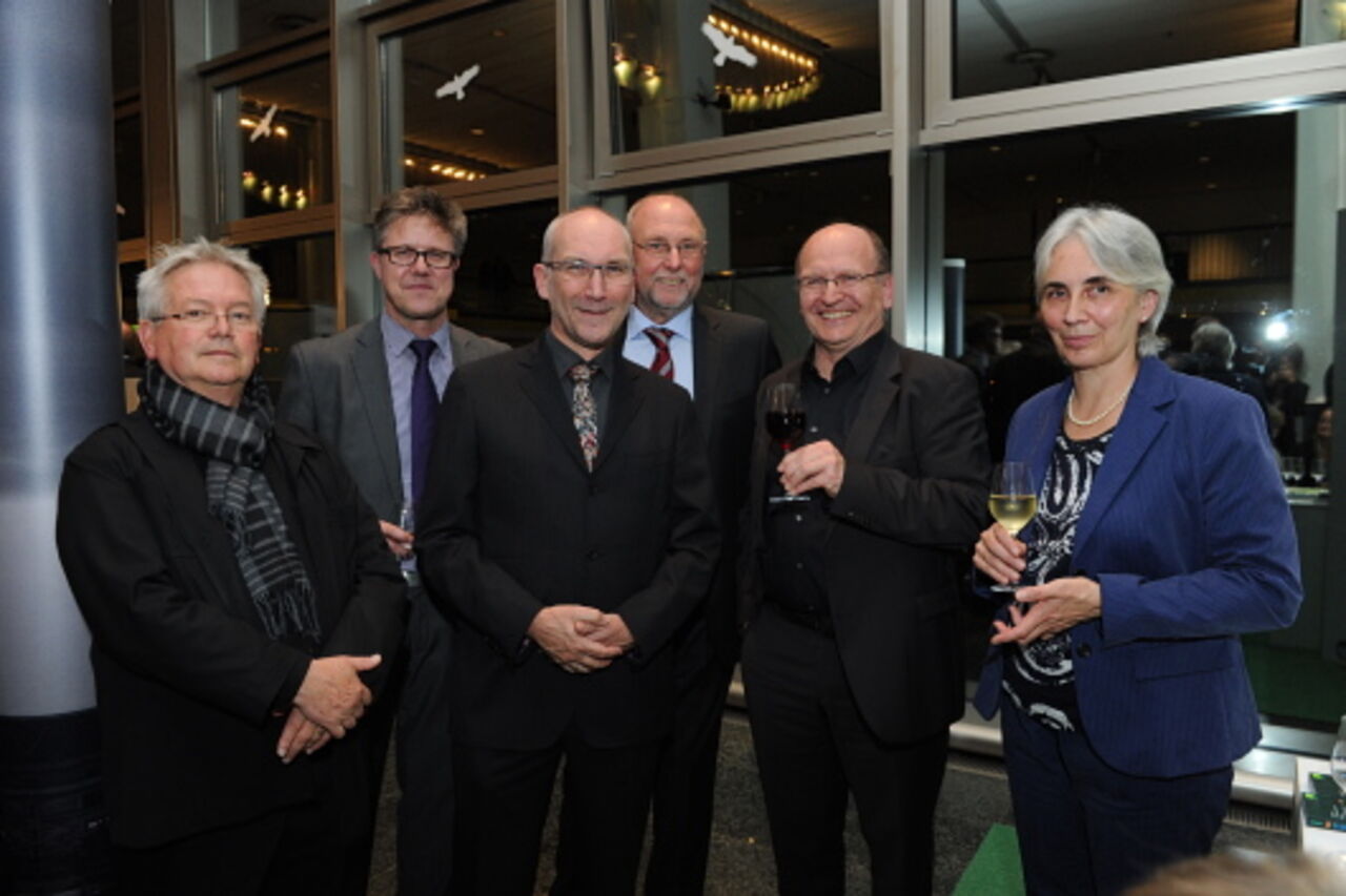 Foto: Vor der Glasfassade posieren fünf Männer und eine Frau zu einem Gruppenbild. 