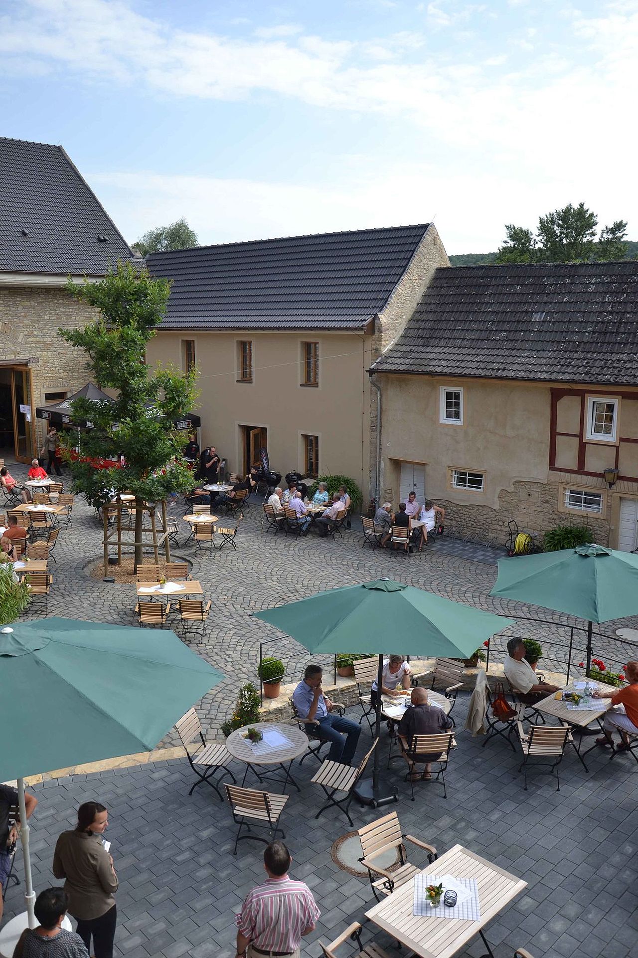 Foto: Blick von der Terrasse in den belebten Innenhof. In der sommerlichen Atmosphäre haben sich viele Gäste eingefunden.