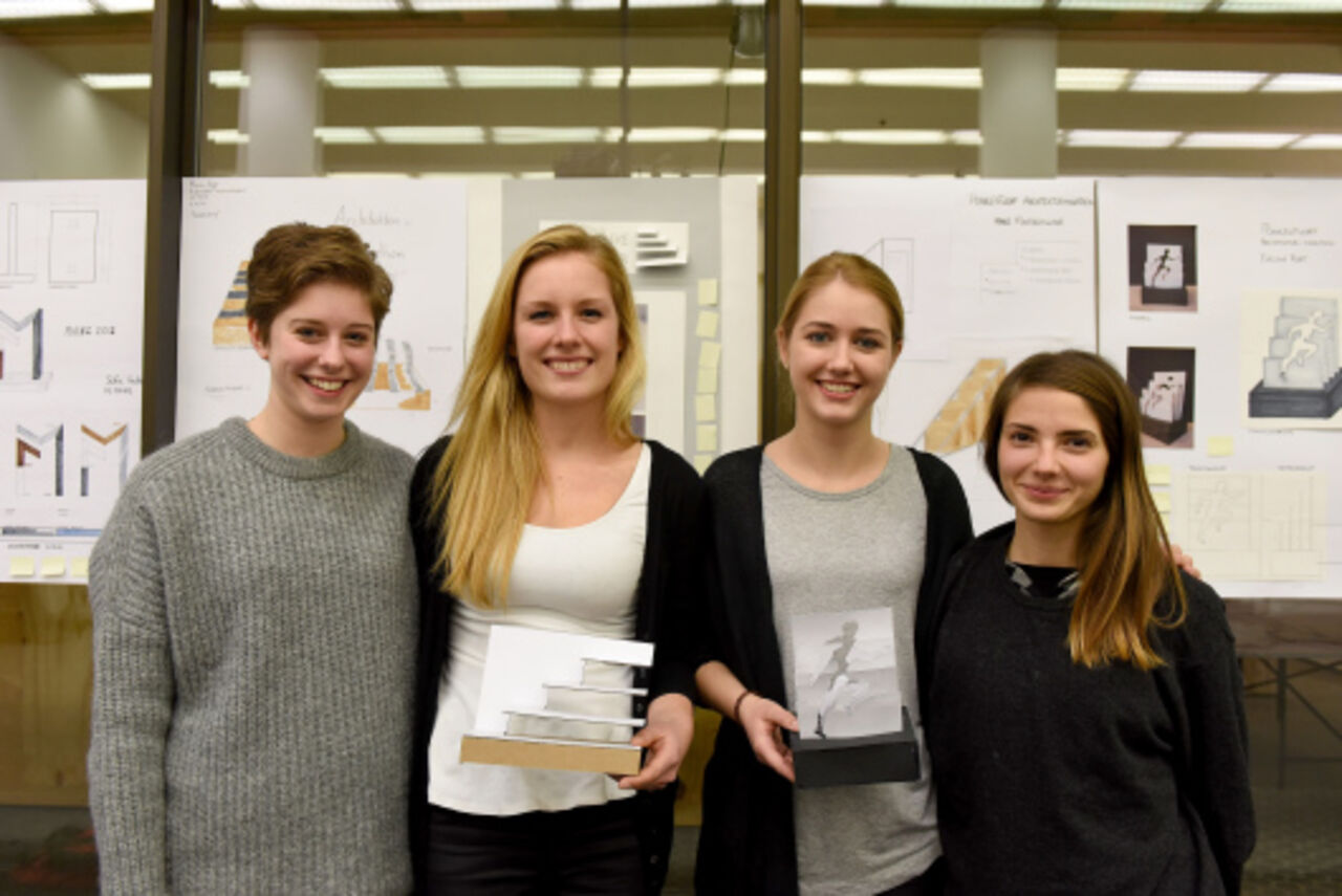 Vier junge Frauen, davon zwei mit einem kleinen Modell ihres Pokalentwurfs in der Hand, lächeln in die Kamera.