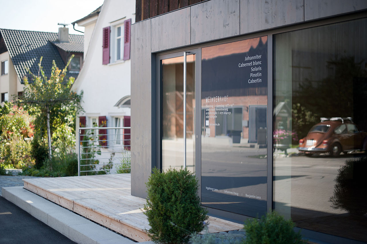 Foto: Blick auf den neuen Eingang mit großer Glastür, der in den neuen Teil der Holzfassade eingelassen ist.