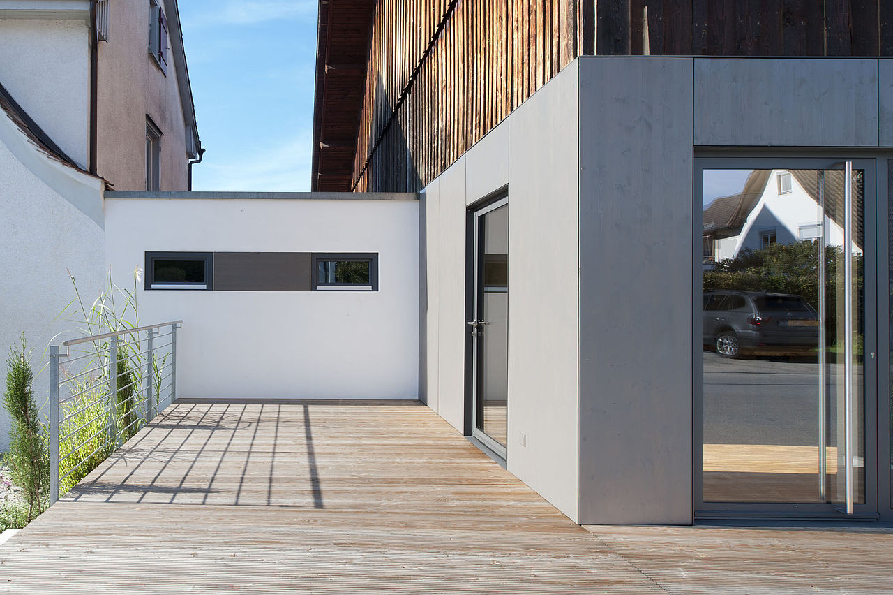 Foto: Blick auf den Verbindungsbau der sich zwischen Wohnhaus und Probierstube befindet. Die Sonne strahlt auf das lichtgraue Holz des ehemaligen Wirtschaftsbaus.