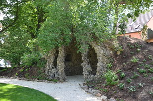 Foto: Grotte aus gekalkten Schlehenwurzeln. Über der Grotte wurde ein Erdhügel angelegt und bepflanzt, daneben befindet sich ein großer Baum.