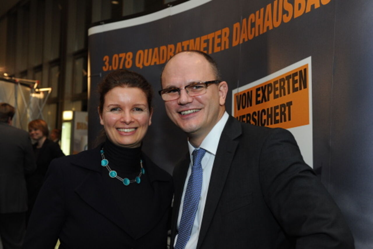 Foto: Eine Frau mit einer auffälligen Halskette und ein Mann im Anzug lächeln in die Kamera.