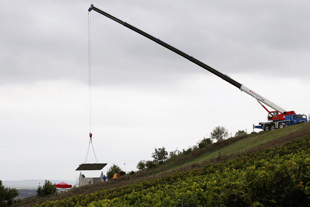 Foto: Anlieferung der Dachelemente aus Beton, welche mit einem Krahn den Hang heruntergelassen werden.