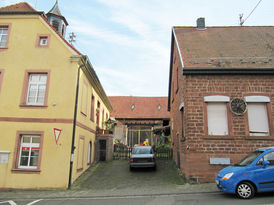 Lücke mit Auto zwischen bäuerlichen Häusern im Ortskern, links in Senfgelb und rechts in Ziegelbauwerk.