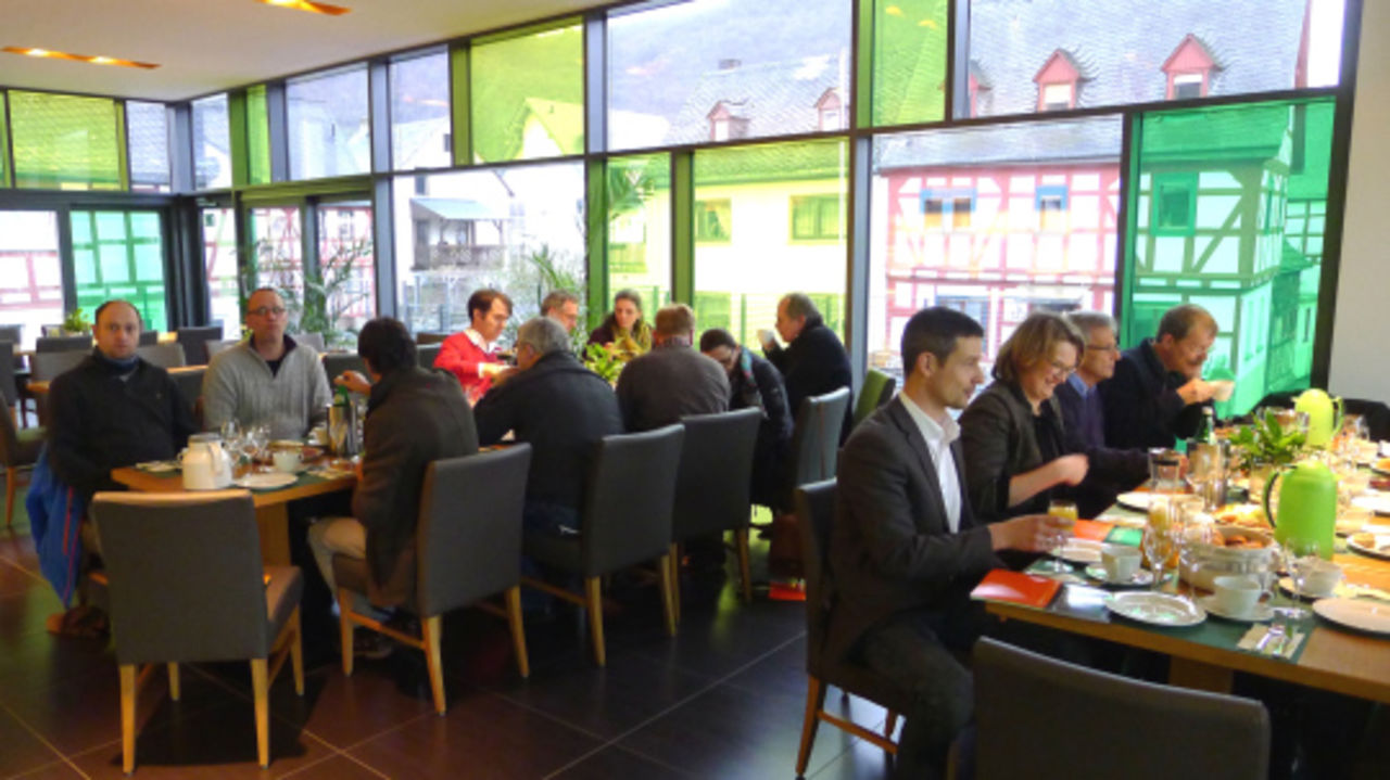Menschen an langen Tischen essen in einem Raum mit vielen farbigen Fenstern