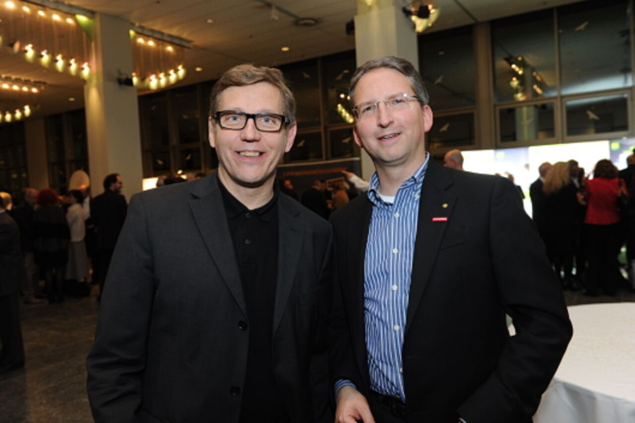 Foto: Zwei Männer mit Hemd und Sacko lächeln in die Kamera.