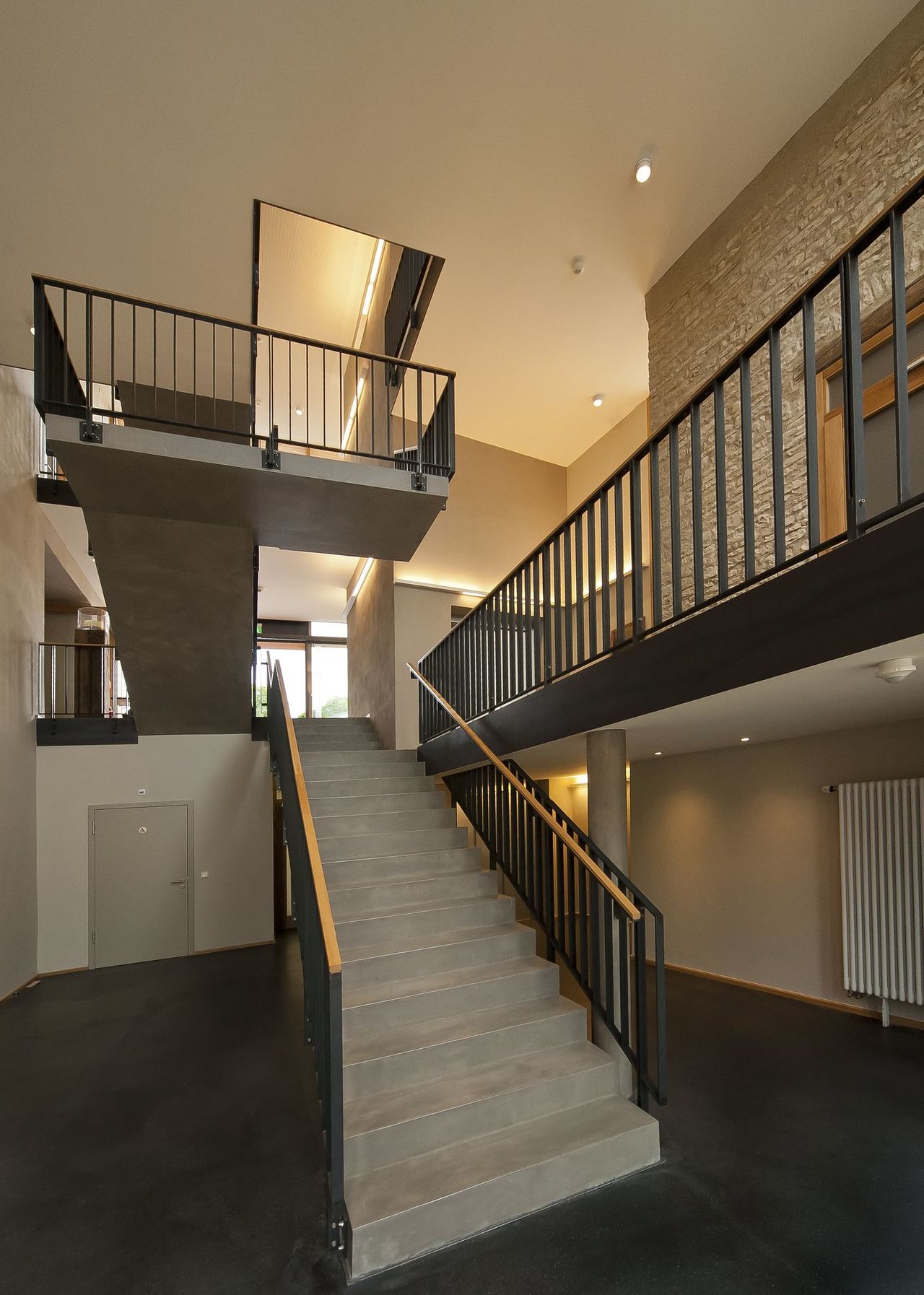 Foto: Blick auf das Treppemhaus des neuen Verbindungsbaus. Die Treppe aus Beton und Stahl fügt sich perfekt in den hohen Raum ein.