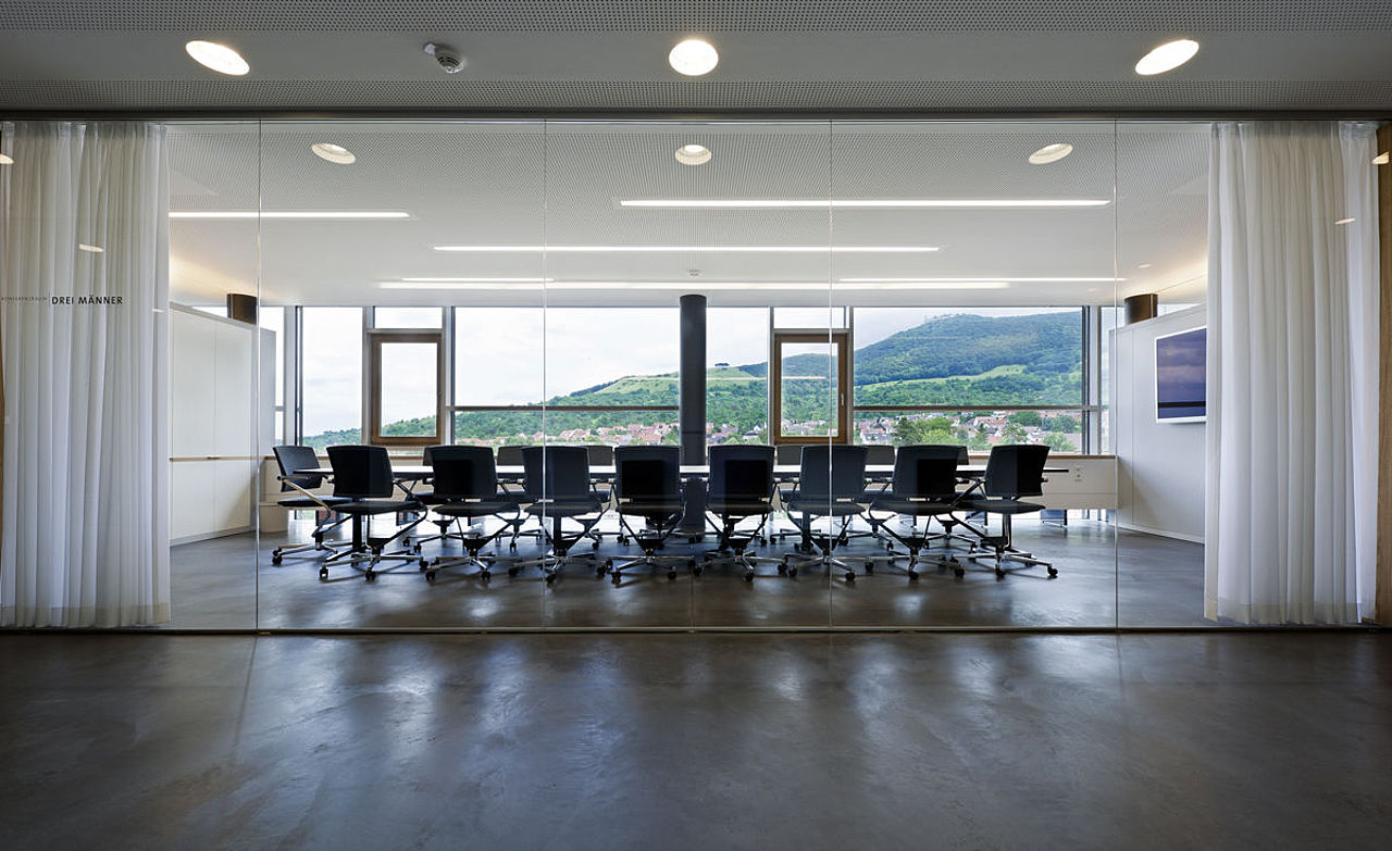 Foto: Blick auf den Konferenzraum, der durch eine bodentiefe Glaswand vom Flur abgetrennt ist. Im Hintergrund sieht man die Landschaft durch die große Glasfassade.