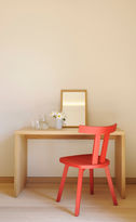 Foto: Blick auf einen schlichten Tisch aus hellem Holz, darauf steht eine Vase mit Margeriten und ein Spiegel. Farblicher Akzent: ein roter Holzstuhl der vor dem Tisch steht.