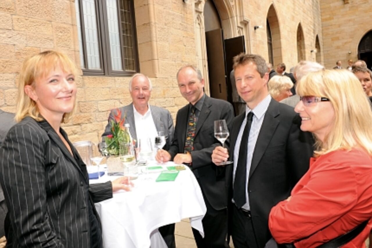 Foto: Fünf Gäste stehen um einen Tisch und lächeln die Fotografin an.