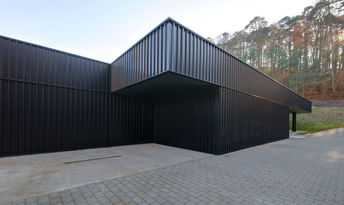 Foto: Bild der schwarzen Fassade ohne Fensteröffnungen, Wald im Hintergrund