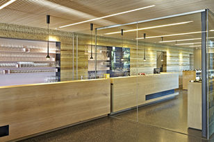 Foto: Langer Tresen aus hellem Holz verbindet Präsentationsraum und Besenwirtschaft, die Räume und der Tresen sind durch ein Glaswand getrennt.