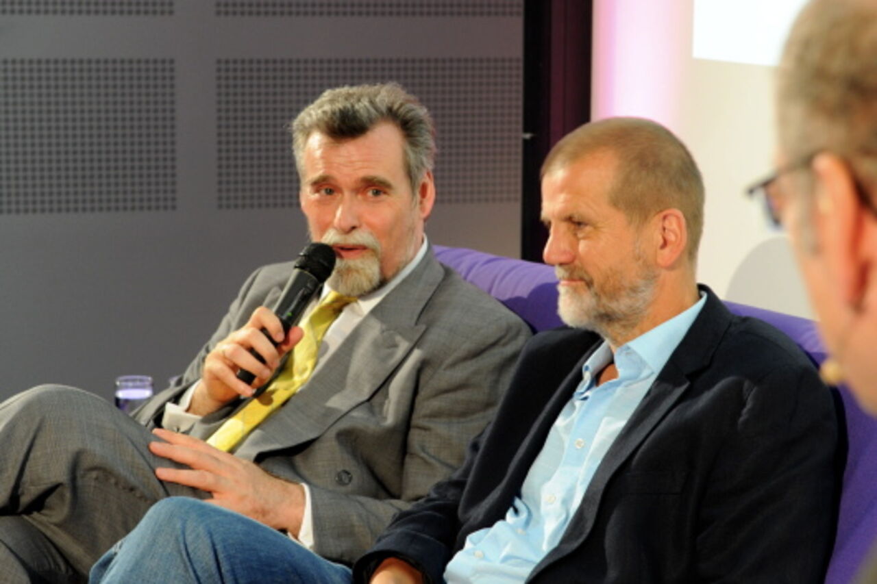 Herbert Mertin sitzend mit Mikrophon auf der Couch mit Jochen Hartloff, vorn rechts der Moderator im Anschnitt