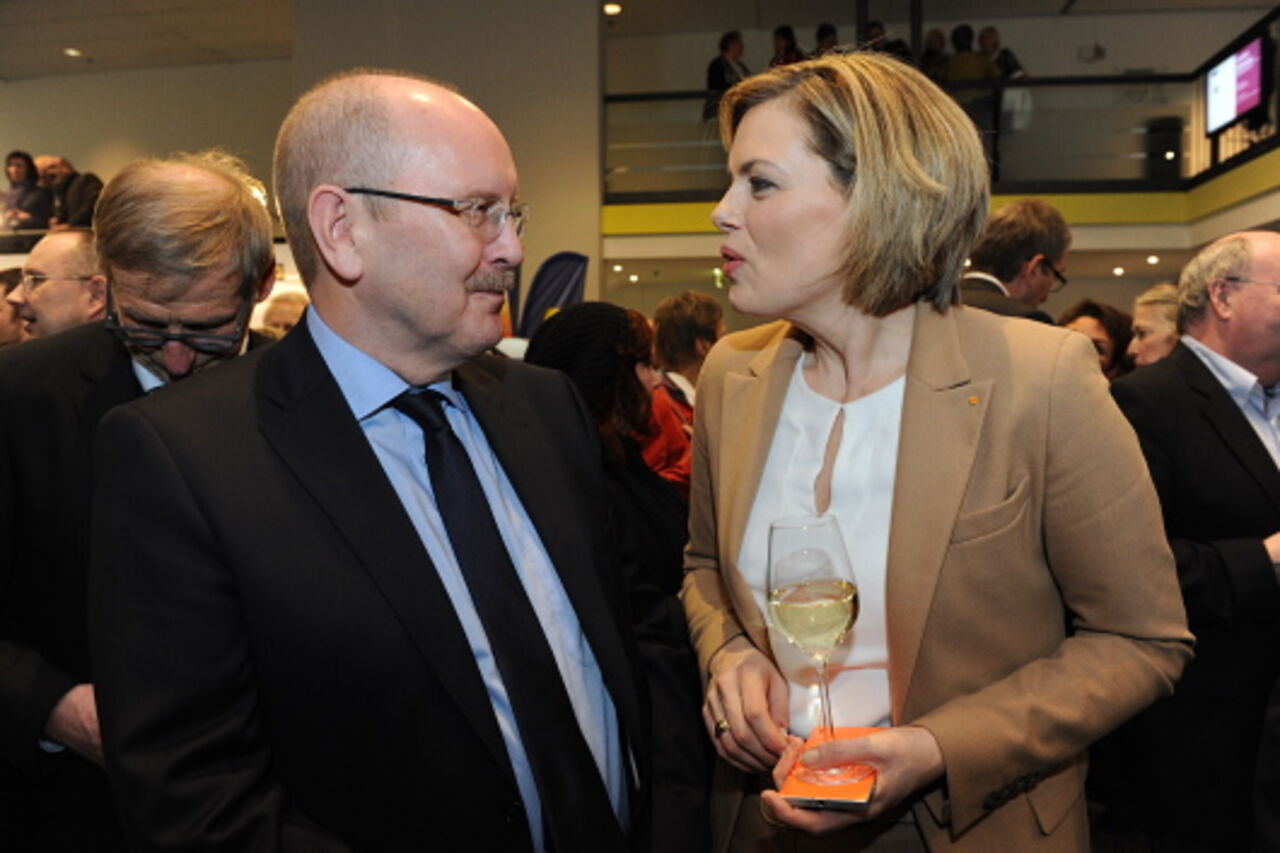 Foto: Ein Mann im Anzug und eine Frau mit einem Glas Wein in der Hand unterhalten sich.