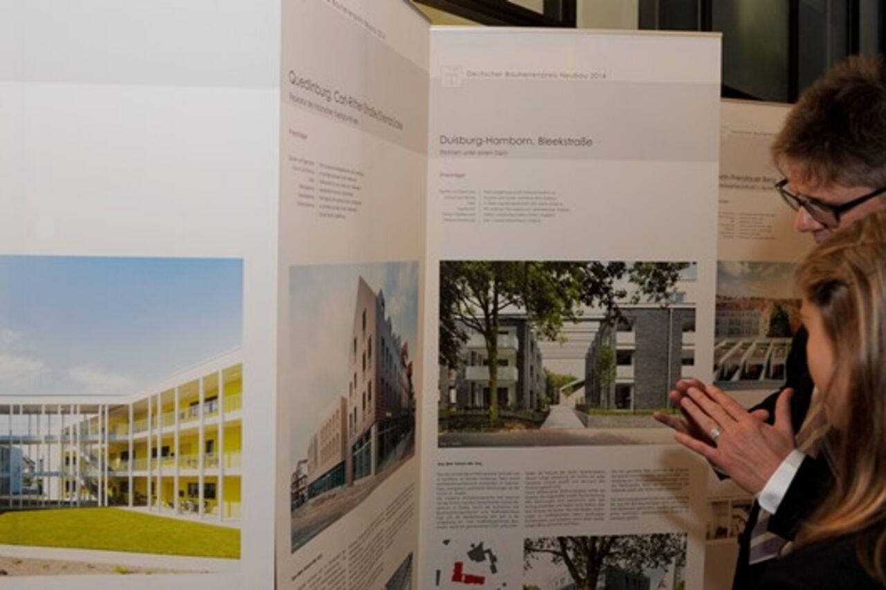 Ausstellungsplakate, rechts im Bild ein Herr und eine junge Frau im Anschnitt vor einem Ausstellungsplakat.