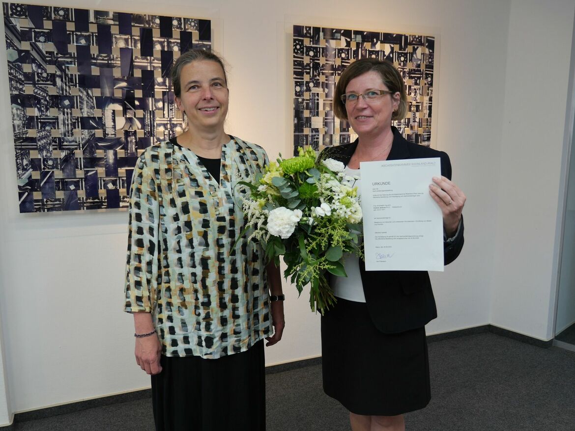 Vizepräsidentin Edda Kurz und Zuzana Jacková Ph.D. stehen nebenainander, Frau Jackova mit dem Blumenstrauß und der Bestallungsurkunde in der Hand.