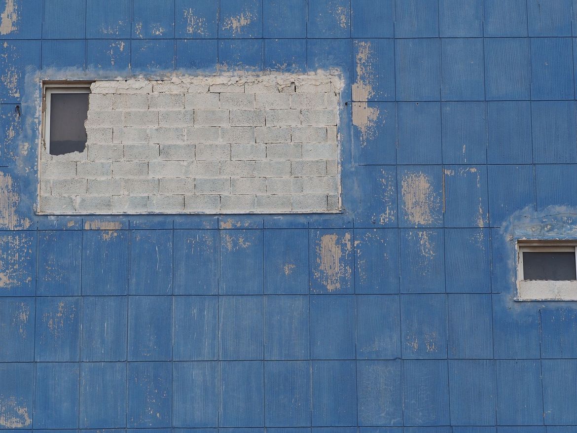 Fassade mit blauen Fsadenelementen und zwei Fensteröffnungen, die zugemauert werden.