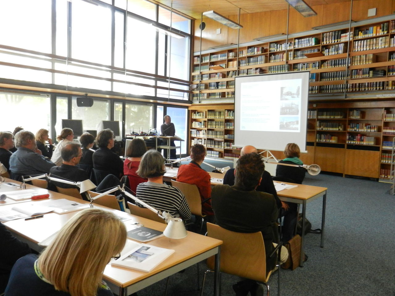 Ein Foto vom Publikum der Veranstaltung mit Blick auf die Präsentation des Sprechers.