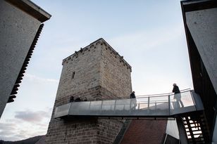 Link im Bild der Burgturm, an dem ein Steg in Metallbauwesie angeschlossen ist, auf dem sich Besucher befinden.