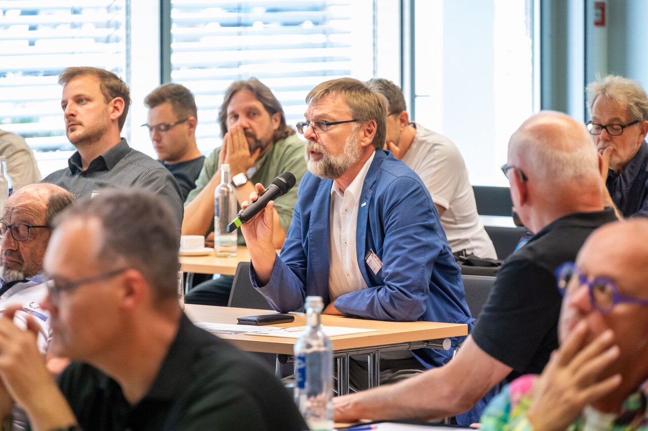 Peter Strokowsky, sitzt im Publikum mit einem Mikro in der Hand und stellt eine Frage