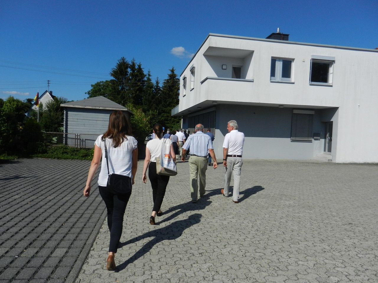 Eine Gruppe von menschen läuft von der Kamera weg, über eine gepflasterte Fläche bei sommerlichem Wetter.