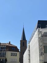 dreiteiliges Foto im Hintergrund eine Kirchen- oder Turmspitze, im Vordergrund eine Fassade verhüllt wegen Bauarbeiten