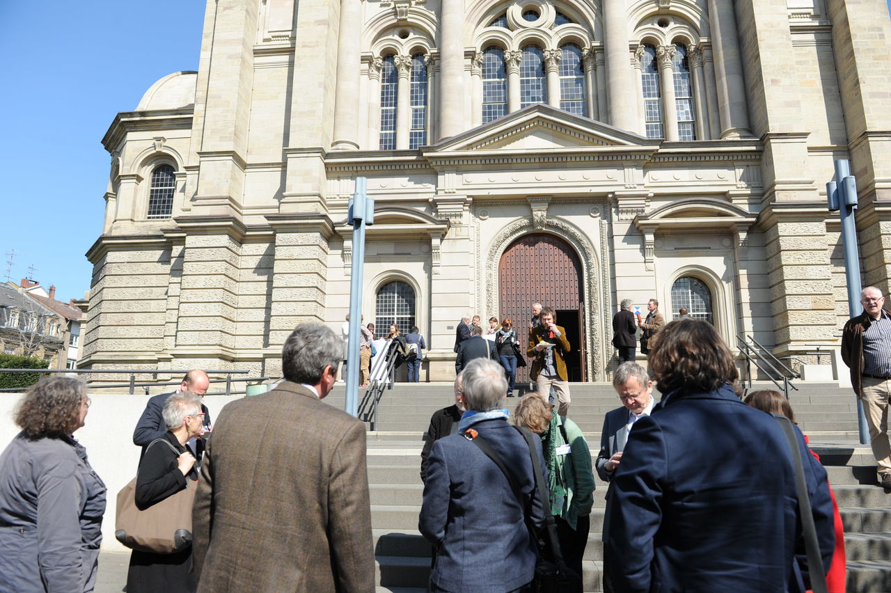 Eine Gruppe von Menschen in Rückansicht, die eine Treppe mit Kirchenfassade betrachten, die Mainzer Christuskirche.