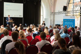 Blick durch die voll besetzten Stuhlreihen zum Rednerpult und zu Staatssekretär Dr. Alexander Wilhelm