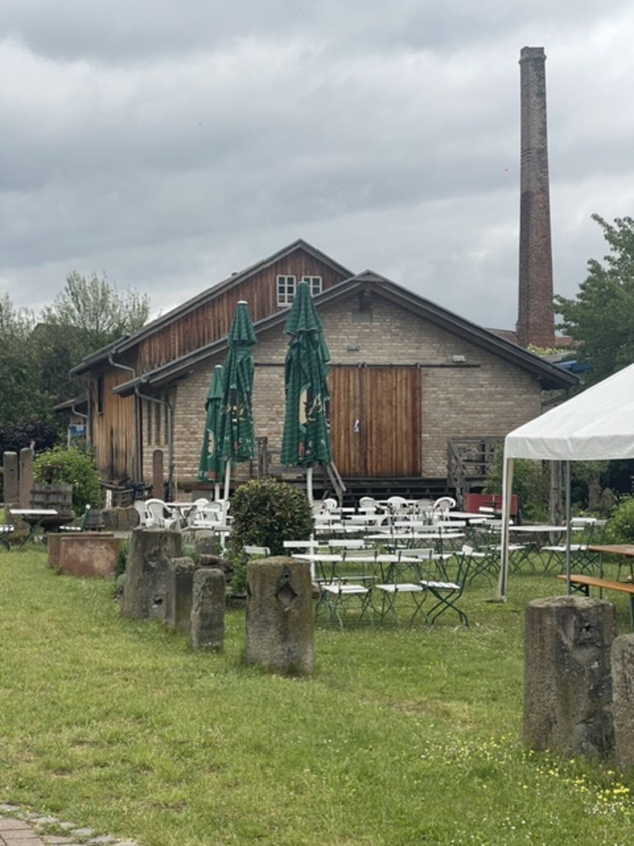 Historisches Gebäude des Alten Sägewerks Bellheim mit Außensitzplätzen und Schornstein.