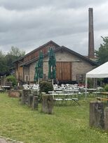 Historisches Gebäude des Alten Sägewerks Bellheim mit Außensitzplätzen und Schornstein.