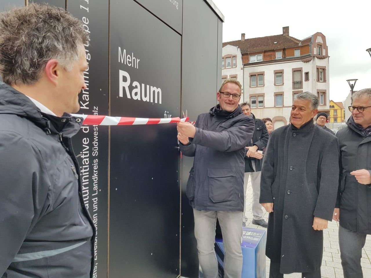 Herr Zwick durchschneidet das Flatterband, das um die Box gebunden ist.