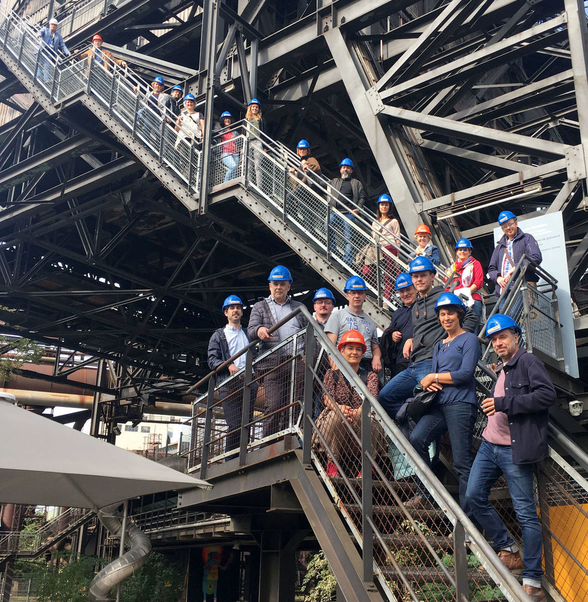 Architektinnen und Architekten mit Helmen stehen auf einer großen Stahltreppenanlage der Völklinger Hütte. 