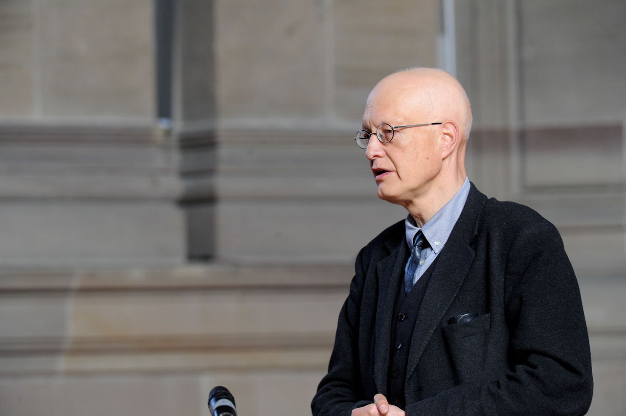 Ein älterer Mann mit kahlem Kopf vor einer der massiven Säulen der Christuskirche.