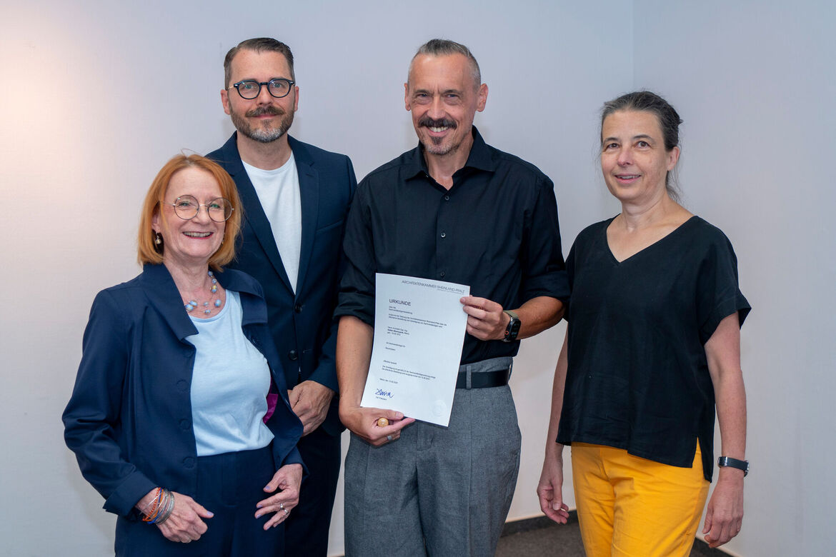 4 Personen stehen vor einer weißen Wand in LGS der AKRP und der neue Sachverständige hält die Bestallungsurkunde und den Rundstempel in der Hand