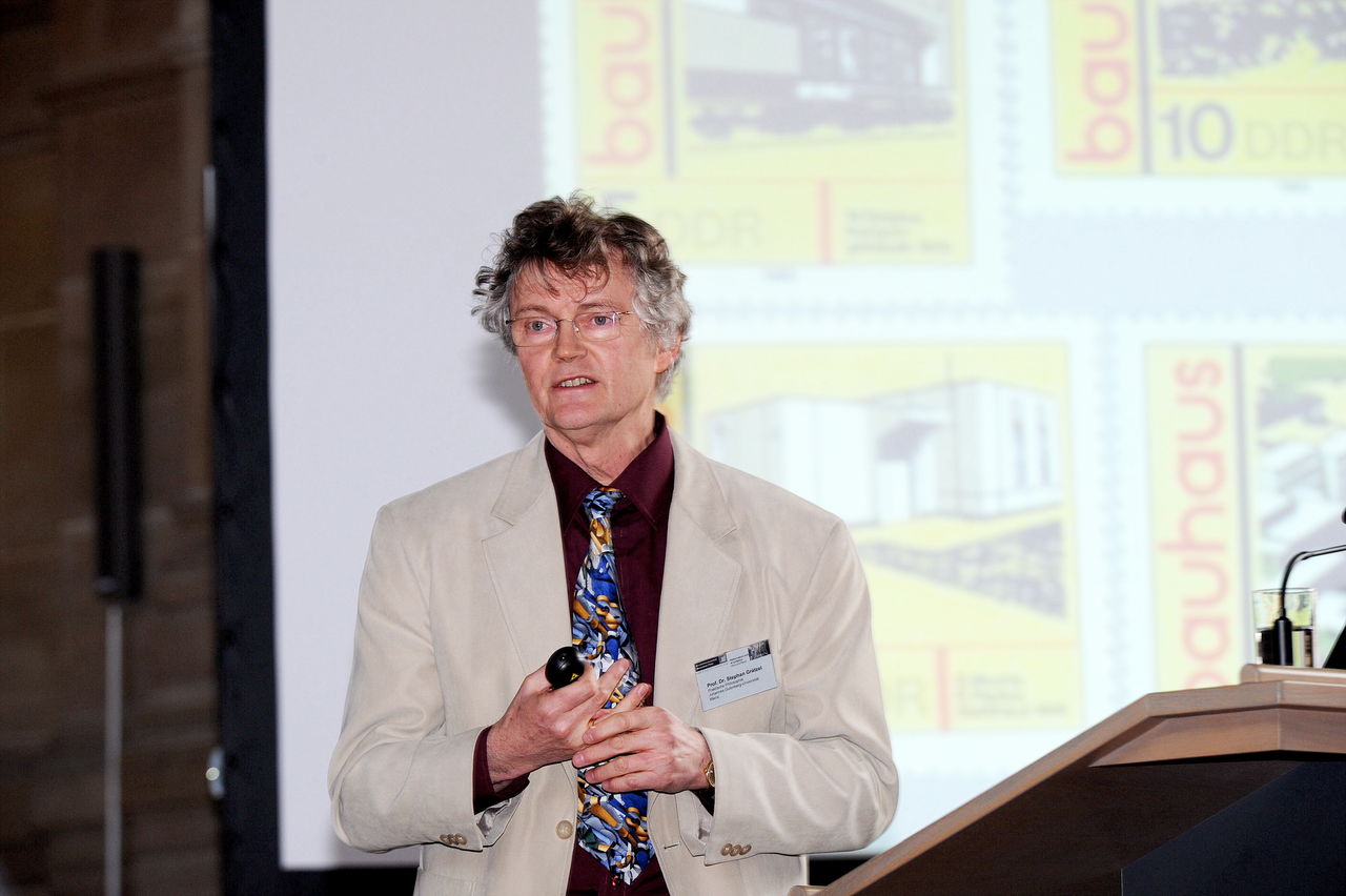Ein Herr mit sandfarbenem Jackett vor einer Präsentation mit Bauhaus Briefmarken.