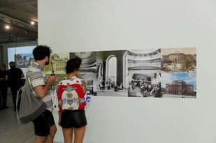 Die Collage zeigtBlick auf die Wand mit Fotos des heutigen Mainzer Staatstheaters aus verschiedenen Zeiten. Im Vordergrund zwei Besucher von hinten die Collage betrachtend.