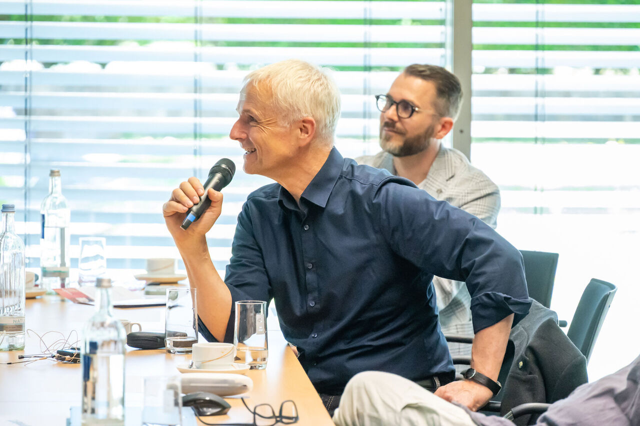 Prof. Zöller sitzt im Publikum mit einem Mikro in der Hand und stellt eine Frage