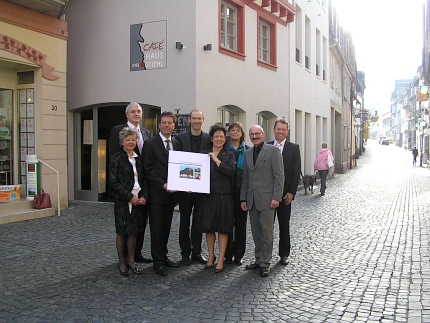 Eine Gruppe von Menschen hält in einer Kopfsteinpflastergasse ein Buch vor sich