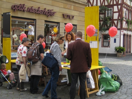 Foto: Menschen stehen um einen gelben Stand in der Fußgängerzone