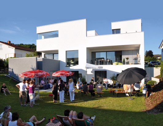 Foto: Andreas Schwickert, Montabaur Foto: strahlend weißes Gebäude vor blauem Himmel, im Vordergrund viele Menschen unter Sonnenschirmen auf dem Rasen, die einem Konzert zuhören.