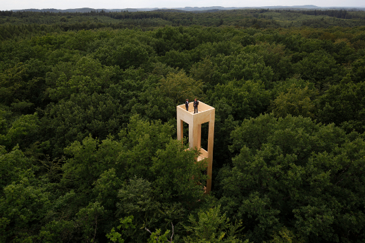 12_MG_0362_SP 530x353_kronenraumforschungsturm.jpg Foto: Blick von einem erhöhten Standort über ein Waldstück, in der Mitte des Bildes befindet sich ein Turm auf dem zwei Menschen stehen